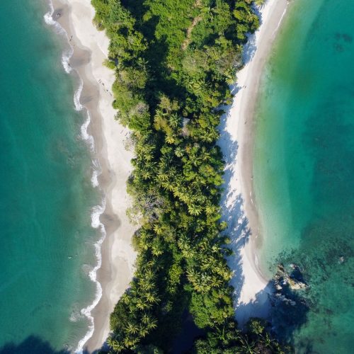 Stunning aerial view of Manuel Antonio Beach with lush green forest and turquoise ocean waters in Costa Rica.
