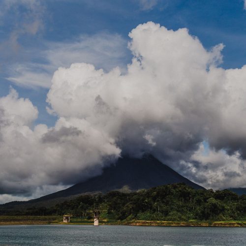 A stunning landscape of Arenal Volcano with clouds and a serene lake view, capturing nature's beauty.