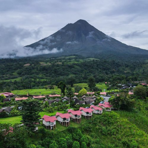 A scenic village with vibrant rooftops nestled below a towering volcano under a cloudy sky.