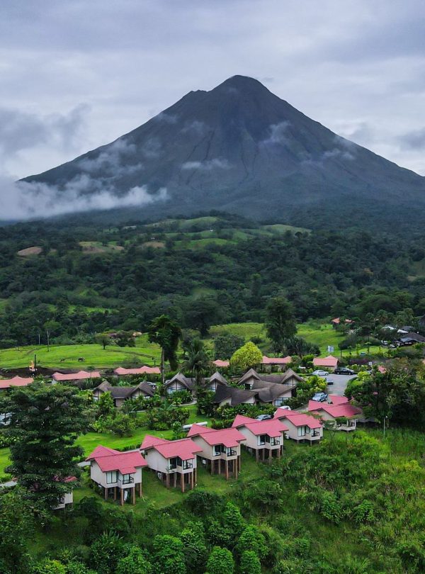 Karibu Kenya Safaris - A scenic village with vibrant rooftops nestled below a towering volcano under a cloudy sky.