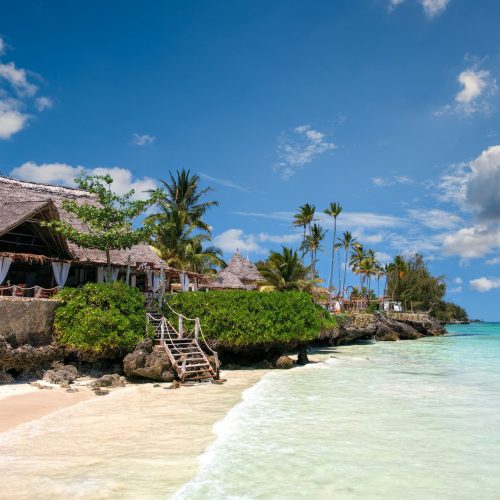 Idyllic beachfront scene in Zanzibar with palm trees, turquoise sea, and a traditional villa.