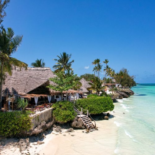 Beautiful tropical beach resort in Zanzibar, Tanzania, with thatched huts, palm trees, and turquoise waters.