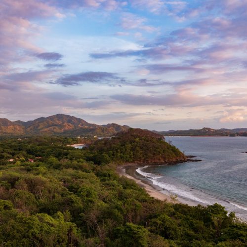 A stunning aerial view of the Guanacaste coastline at sunset with lush greenery and gentle waves.