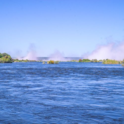 Beautiful river scene with mist, vibrant greenery, and clear blue sky.